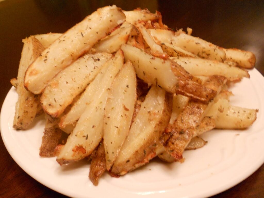 A plate piled with golden-brown Easy Oven Fries, seasoned with herbs and baked to perfection, served on a white dish.