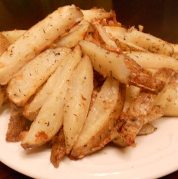 A plate piled with golden-brown Easy Oven Fries, seasoned with herbs and baked to perfection, served on a white dish.