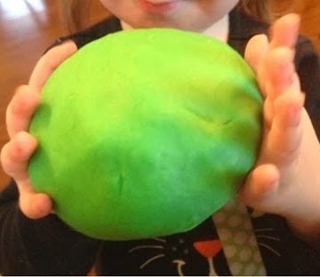 child's hands holding green homemade play dough