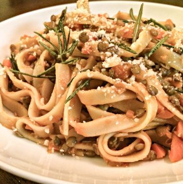 A close-up of fettuccine pasta topped with a hearty Lentil Bolognese—diced carrots, fresh rosemary, and grated cheese—served on a white plate, showcasing a flavorful vegan pasta sauce.
