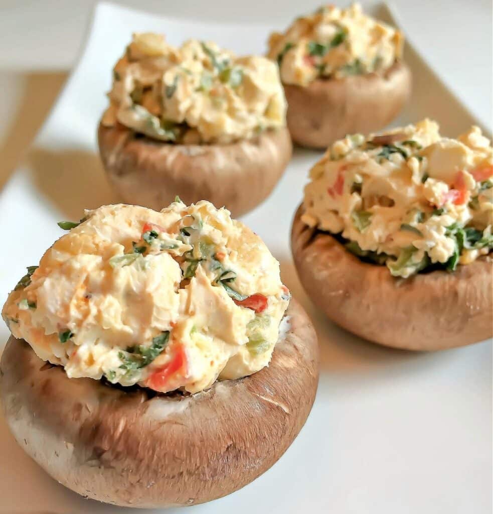 Four large Cajun Spiced Stuffed Mushrooms filled with a creamy blend of herbs, cheese, and diced vegetables, arranged elegantly on a white rectangular plate.