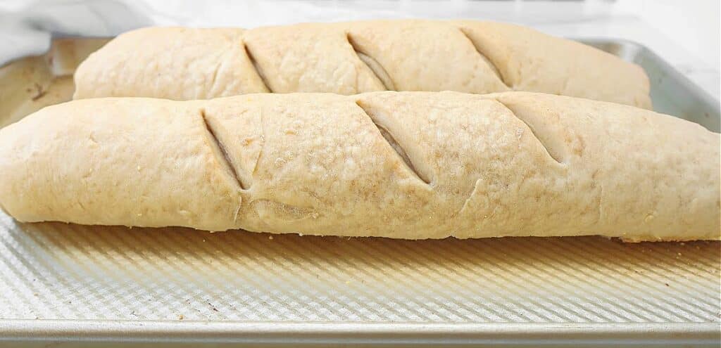 Two loaves of homemade French bread baguette with slits on top rest on a baking sheet, perfect for an easy, quick bake.