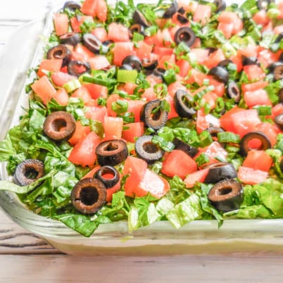 Vegan 7-Layer Party Dip - Seven layers of taco-spiced refried beans, homemade guacamole, vegan sour cream, lettuce, tomatoes, black olives, & green onions.