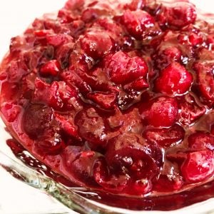 Close-up of a glass bowl filled with chunky Thanksgiving cranberry sauce, featuring whole and partially crushed cranberries in a glossy, deep red sauce.