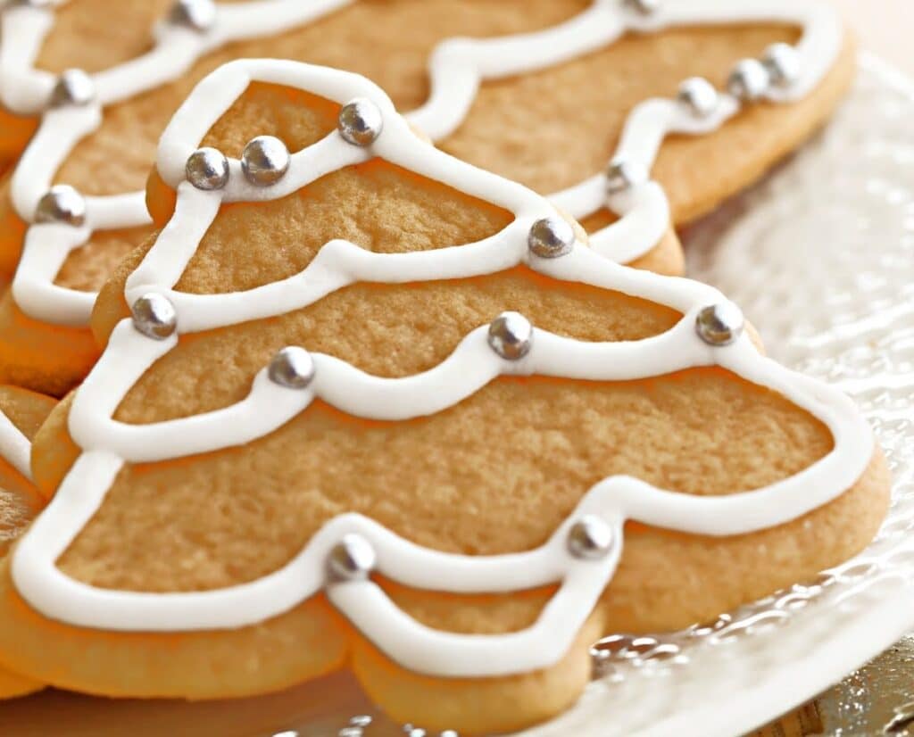 Christmas tree-shaped sugar cookie decorated with vegan royal icing and silver candy pearls, placed on a clear glass plate.