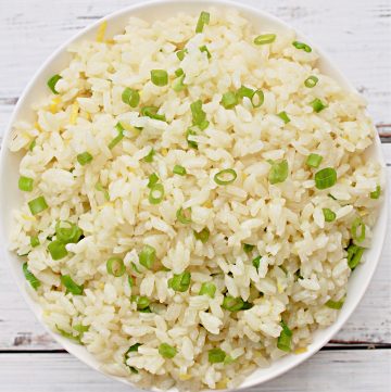 A bowl of scallion rice garnished with chopped green onions, placed on a white wooden surface.