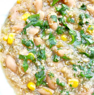A close-up of a hearty white bean quinoa chili soup with corn and fresh herbs, served in a white bowl. The thick stew features visible grains, beans, and vibrant vegetables for a wholesome meal.