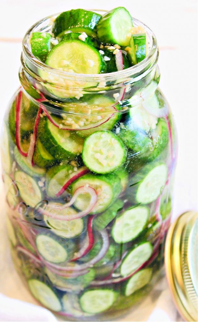 Open glass ar stuffed with cucumbers, onion, garlic, and pickling brine. 