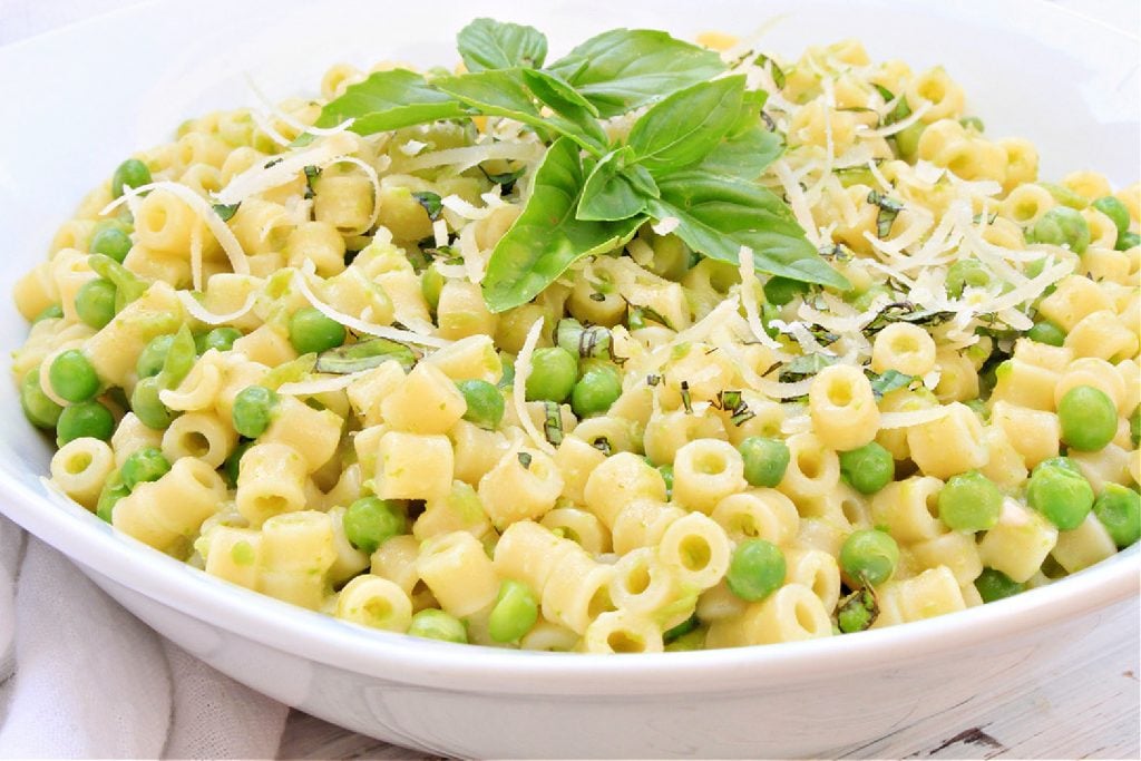 Pasta with peas topped with fresh basil in white bowl.