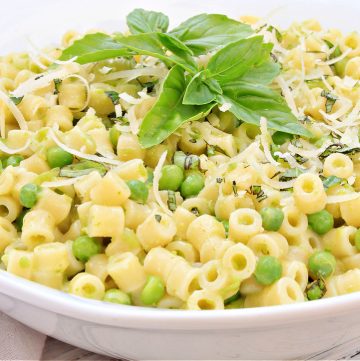 Pasta with peas topped with fresh basil in white bowl.