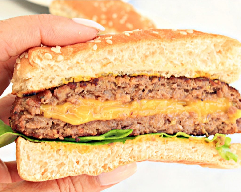 Hand holding burger cut in half to show cheese.