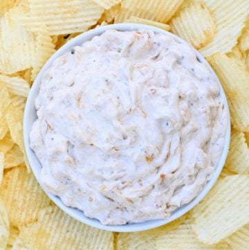 A bowl of creamy french onion dip sits in the center of a plate, surrounded by ridged potato chips—perfect for sharing this classic French Onion Dip Recipe at your next gathering.