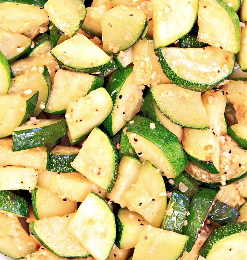 Garlic butter zucchini slices are sautéed and seasoned with black pepper and spices, arranged closely together and glistening with a light coating of oil.