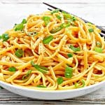 A plate of delicious garlic sesame noodles, coated in a rich and flavorful sauce made with garlic, soy sauce, sesame oil, and other spices. The noodles are garnished with sliced green onions and sesame seeds for added texture and flavor. This easy-to-make dish is perfect for a quick and satisfying meal.