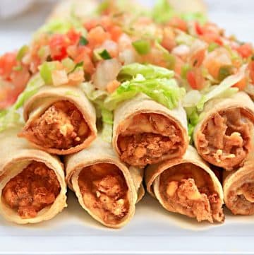 A close-up of six crispy bean and cheese taquitos filled with seasoned meat, arranged in a row on a white plate, garnished with shredded lettuce and fresh pico de gallo.