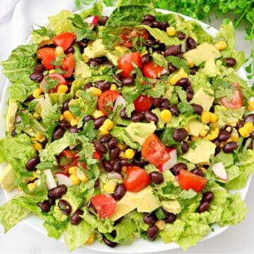 A fresh Mexican chopped salad featuring romaine lettuce, black beans, corn, diced avocado, cherry tomatoes, red onion, and cilantro, all served in a white bowl.