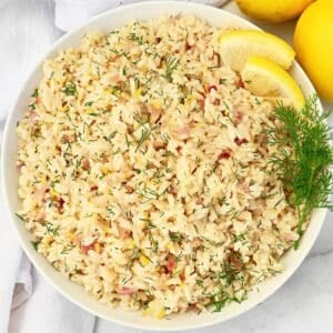 A bowl of lemon rice garnished with fresh dill and lemon slices, viewed from above. The rice is mixed with herbs and small bits of vegetables, creating a colorful and appetizing presentation.