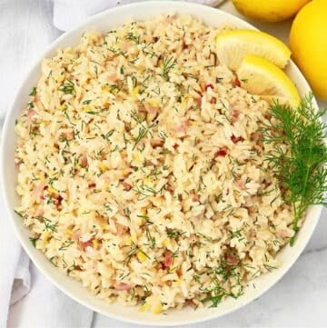 A bowl of lemon rice garnished with fresh dill and lemon slices, viewed from above. The rice is mixed with herbs and small bits of vegetables, creating a colorful and appetizing presentation.