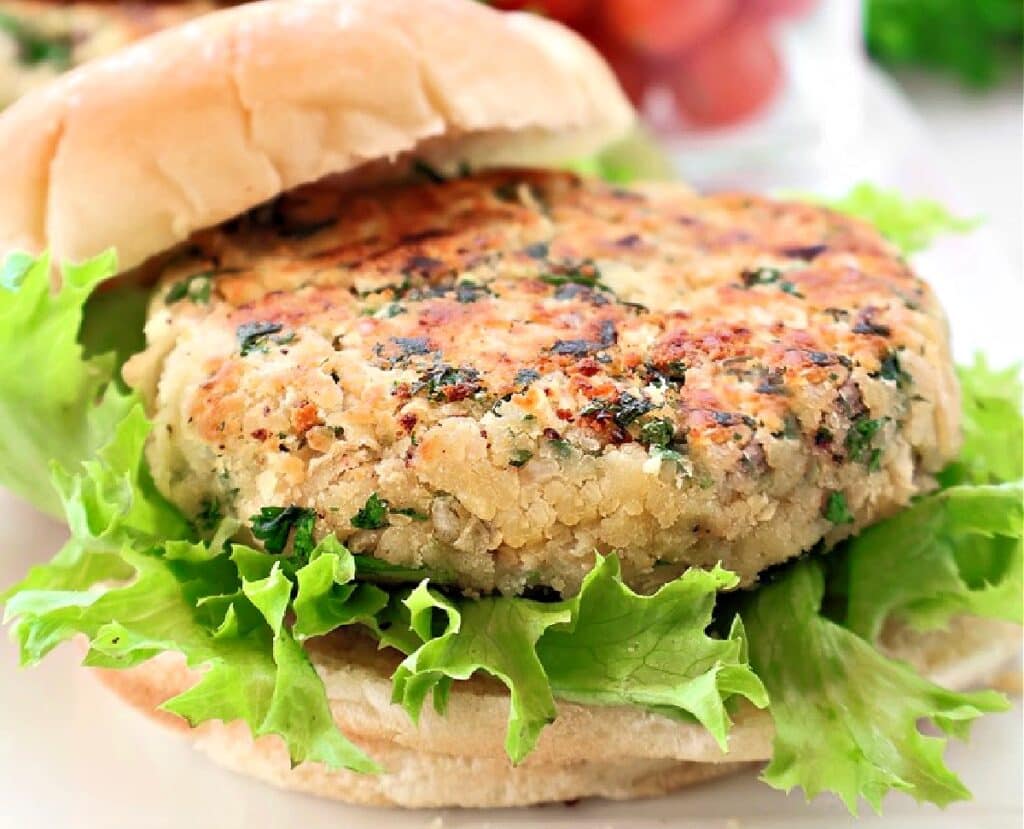 A close-up of a veggie burger with a chickpea patty, fresh green leaf lettuce, and a soft hamburger bun. The patty is lightly browned and speckled with herbs.