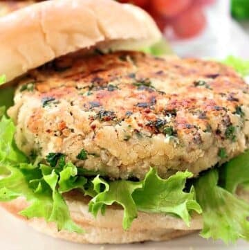 A close-up of a veggie burger with a chickpea patty, fresh green leaf lettuce, and a soft hamburger bun. The patty is lightly browned and speckled with herbs.