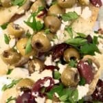 Close-up of focaccia bread topped with green and kalamata olives, crumbled feta cheese, and fresh chopped parsley.