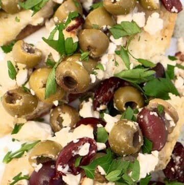 Close-up of focaccia bread topped with green and kalamata olives, crumbled feta cheese, and fresh chopped parsley.