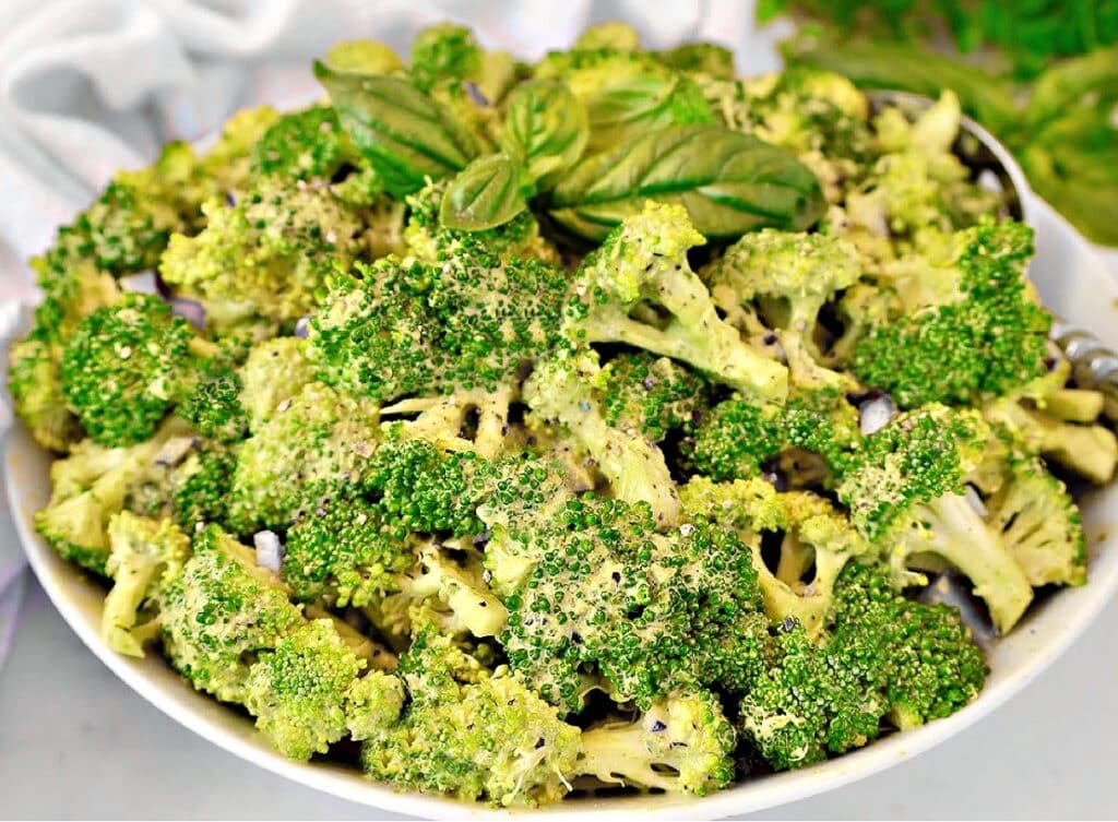 A white bowl filled with fresh broccoli florets, garnished with chopped herbs and topped with a sprig of basil.