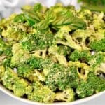 A white bowl filled with fresh broccoli florets, garnished with chopped herbs and topped with a sprig of basil.