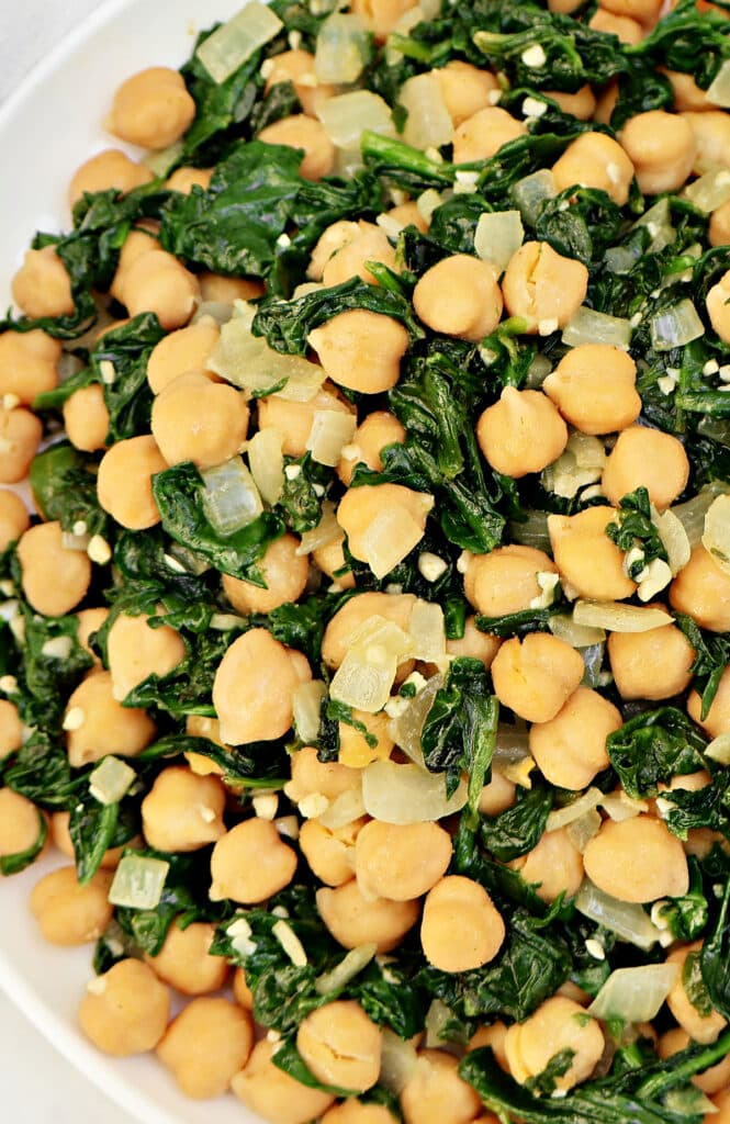 A plate filled with cooked chickpeas, sautéed spinach, chopped onions, and minced garlic, all mixed together.