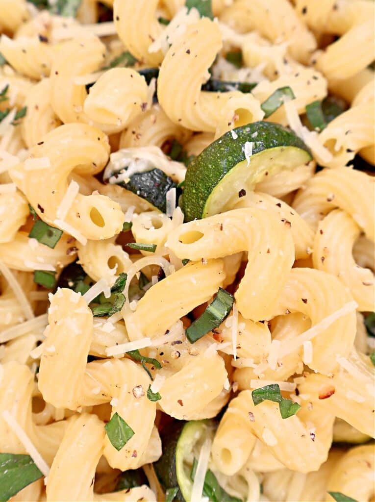 Close-up of curly pasta mixed with zucchini slices, grated Parmesan cheese, fresh basil, and cracked black pepper.