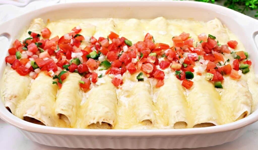 A baking dish filled with cheesy enchiladas, topped with melted cheese and a fresh tomato, onion, and cilantro salsa down the center.