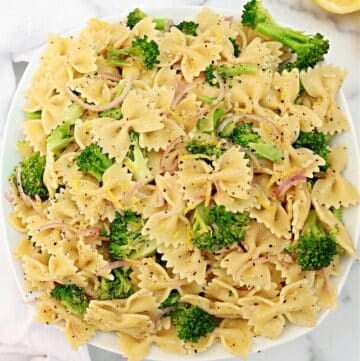A white plate filled with bowtie pasta mixed with broccoli florets and thinly sliced red onions, lightly seasoned with black pepper.