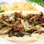 A close-up of a mushroom sandwich with melted cheese, sautéed onions, green peppers, and parsley on a hoagie roll—served alongside potato chips. Great for fans of classic fare or hearty portobello mushroom sandwiches.