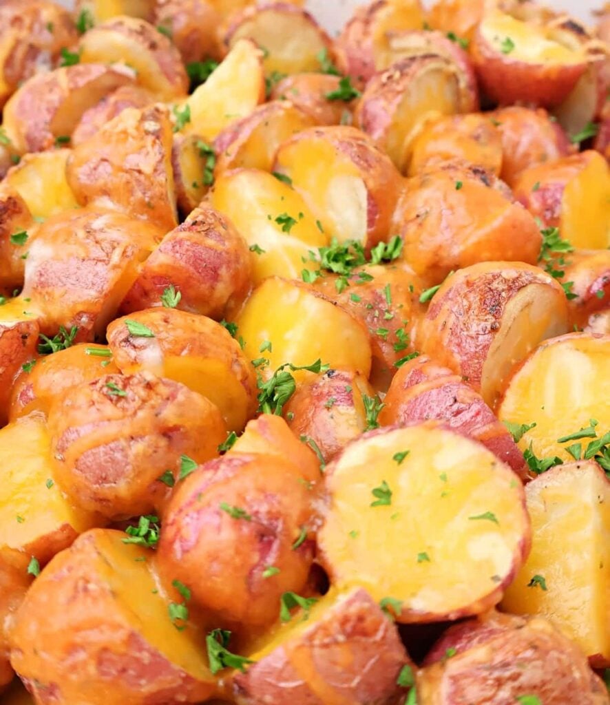 Halved red potatoes baked with melted cheddar cheese, garnished with chopped parsley, shown close-up in a serving dish.