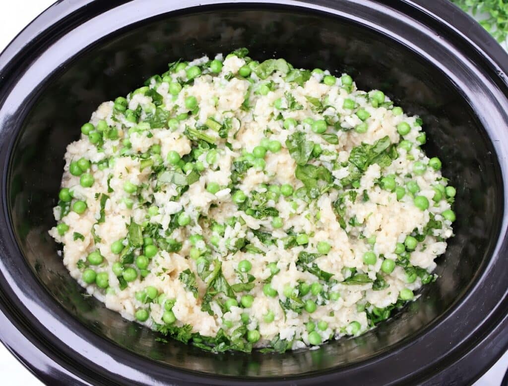 A slow cooker risotto filled with creamy rice, green peas, and chopped fresh herbs creates a colorful and appetizing dish.