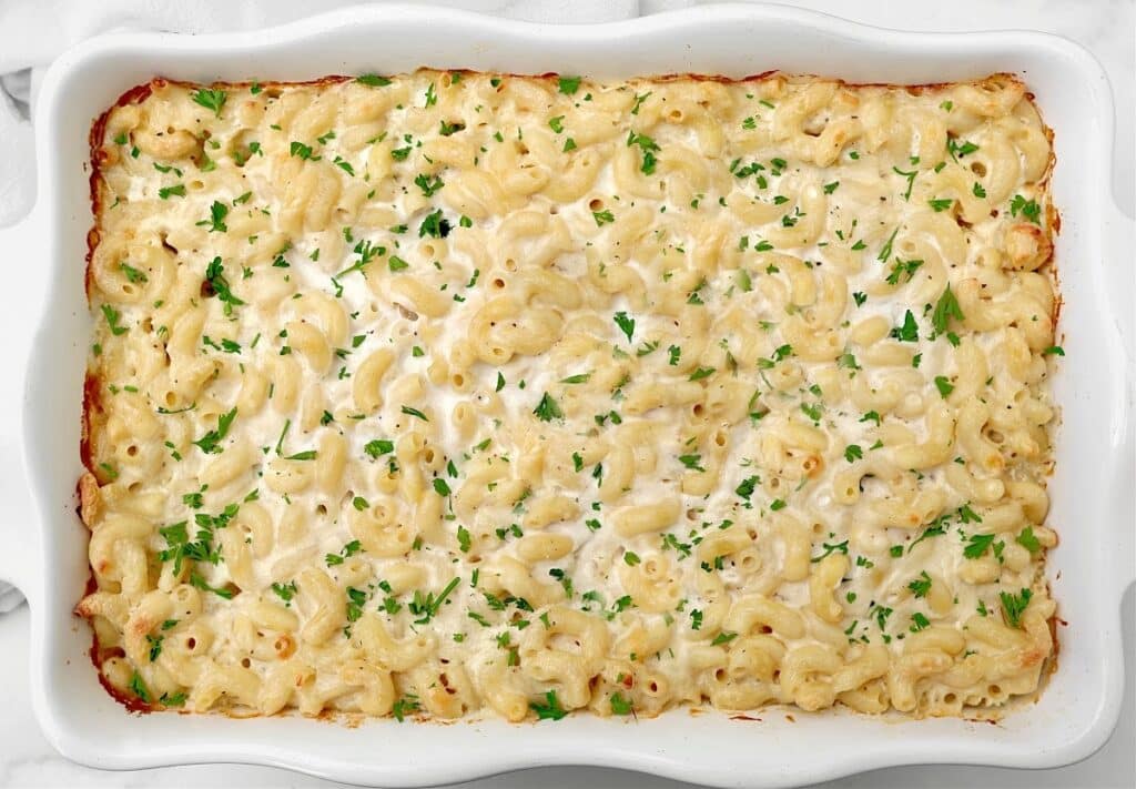 A make ahead mac and cheese casserole in a white dish, topped with melted cheese and sprinkled with chopped parsley.