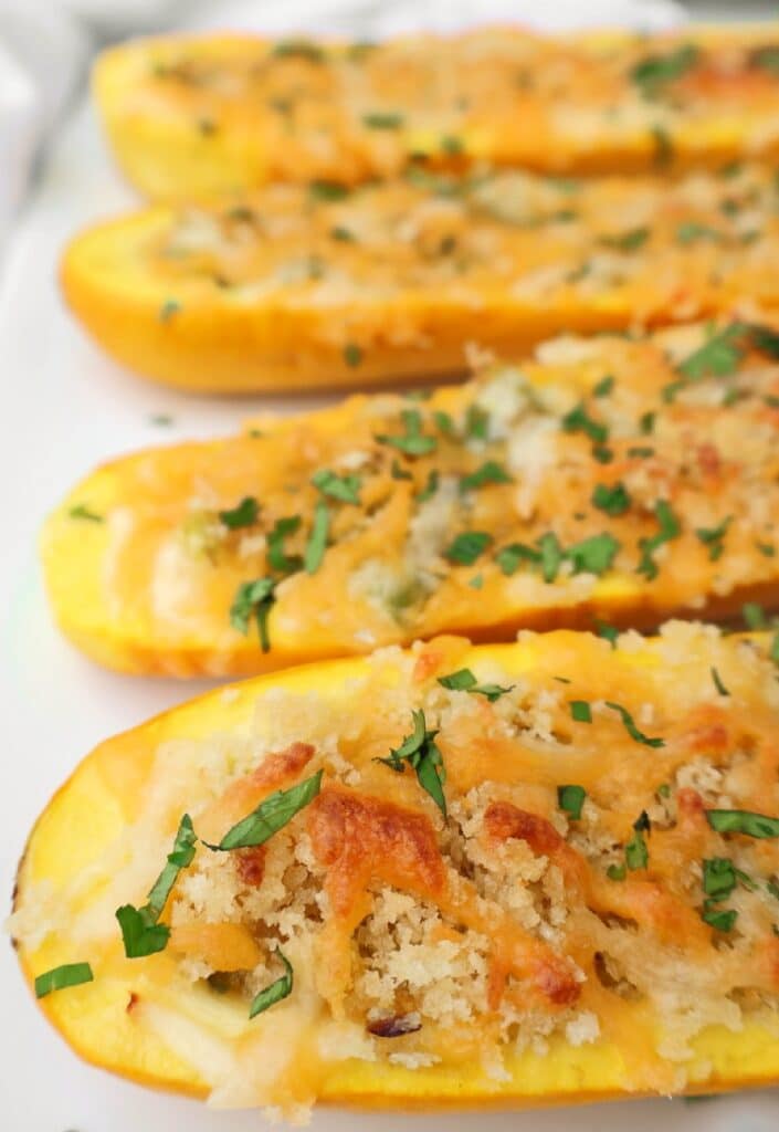 Close-up of stuffed yellow squash halves topped with a golden, crispy breadcrumb and cheese mixture, garnished with chopped fresh herbs on a white plate.