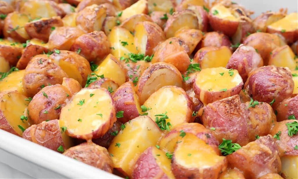 Roasted red potatoes cut in halves, topped with melted cheese and sprinkled with fresh chopped parsley, served in a white dish.