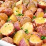 Roasted red potatoes cut in halves, topped with melted cheese and sprinkled with fresh chopped parsley, served in a white dish.