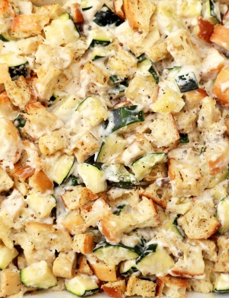 A close-up of a baked casserole with chunks of bread, zucchini, and melted cheese, all seasoned and mixed together for a savory, golden-brown dish.