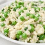 Creamy slow cooker risotto with bright green peas and fresh herbs, served on a white plate. The rice appears tender and slightly glossy, with peas evenly distributed throughout.