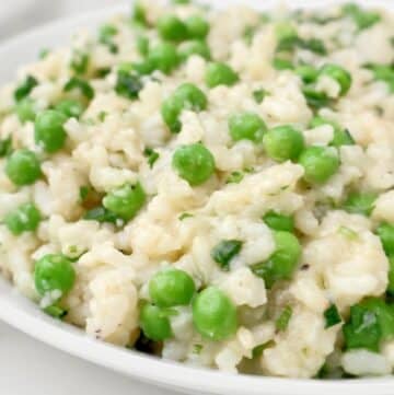 Creamy slow cooker risotto with bright green peas and fresh herbs, served on a white plate. The rice appears tender and slightly glossy, with peas evenly distributed throughout.
