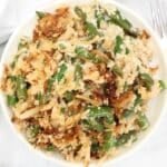 A bowl filled with green bean casserole, topped with crispy fried onions and breadcrumbs, mixed with creamy sauce and green beans.