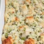 A close-up of a baked bread stuffing casserole in a white dish, featuring golden brown bread cubes mixed with herbs and celery.