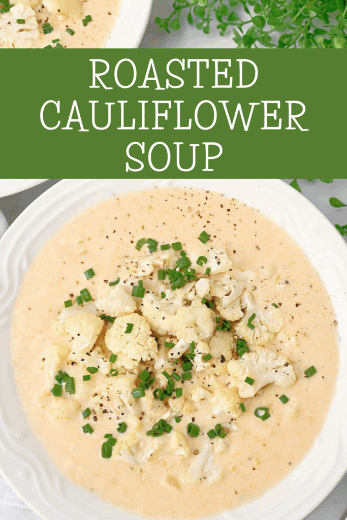 A bowl of creamy roasted cauliflower soup topped with roasted cauliflower florets and chopped chives, served in a white bowl. Text above reads Roasted Cauliflower Soup on a green background.