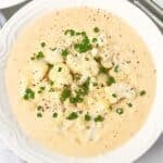 A bowl of creamy cauliflower soup, garnished with chopped chives and black pepper, served in a white dish.