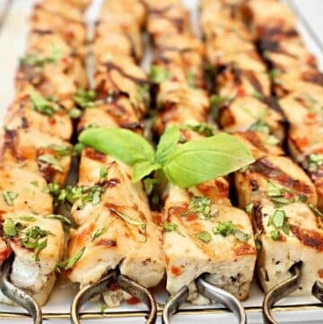Grilled tofu skewers topped with chopped herbs are arranged on a platter, garnished with fresh basil leaves in the center. The meat is golden brown with visible grill marks.