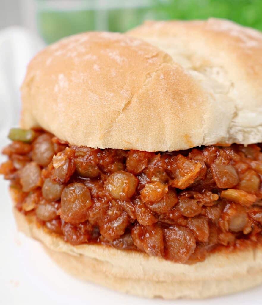 A close-up of a sandwich with a soft bun filled with a hearty lentil-based sloppy joe mixture in a rich, red sauce.