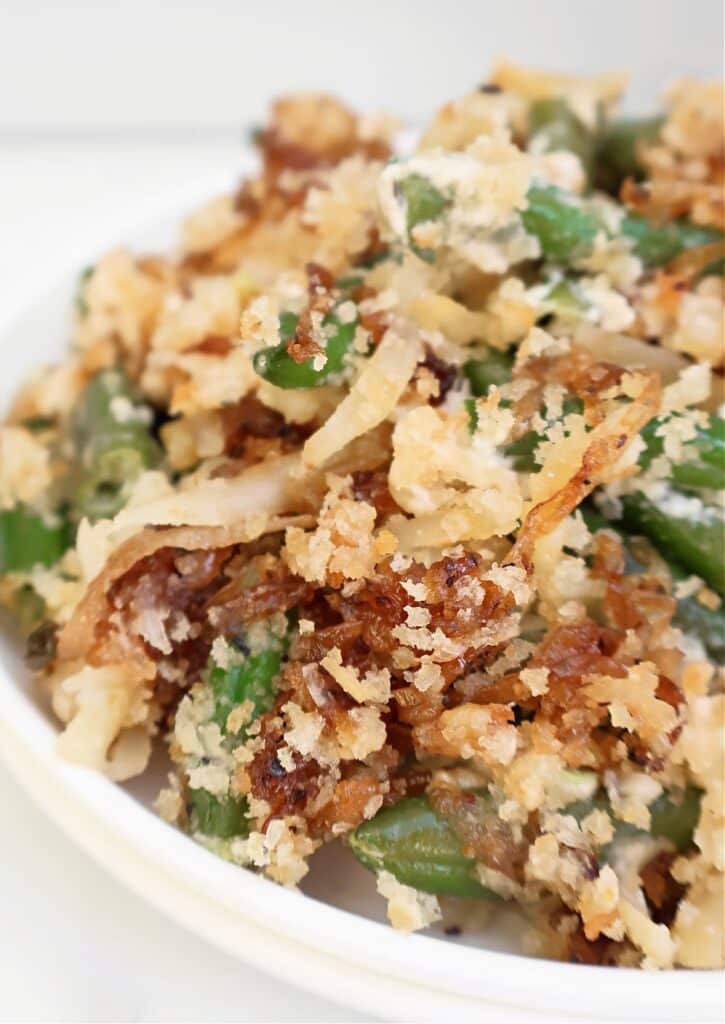 A close-up of a serving of green bean casserole topped with crispy fried onions and breadcrumbs on a white plate.