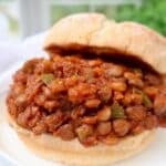 A close-up of a sandwich filled with a hearty lentil and vegetable mixture in a tomato-based sauce, served on a soft, round bun.